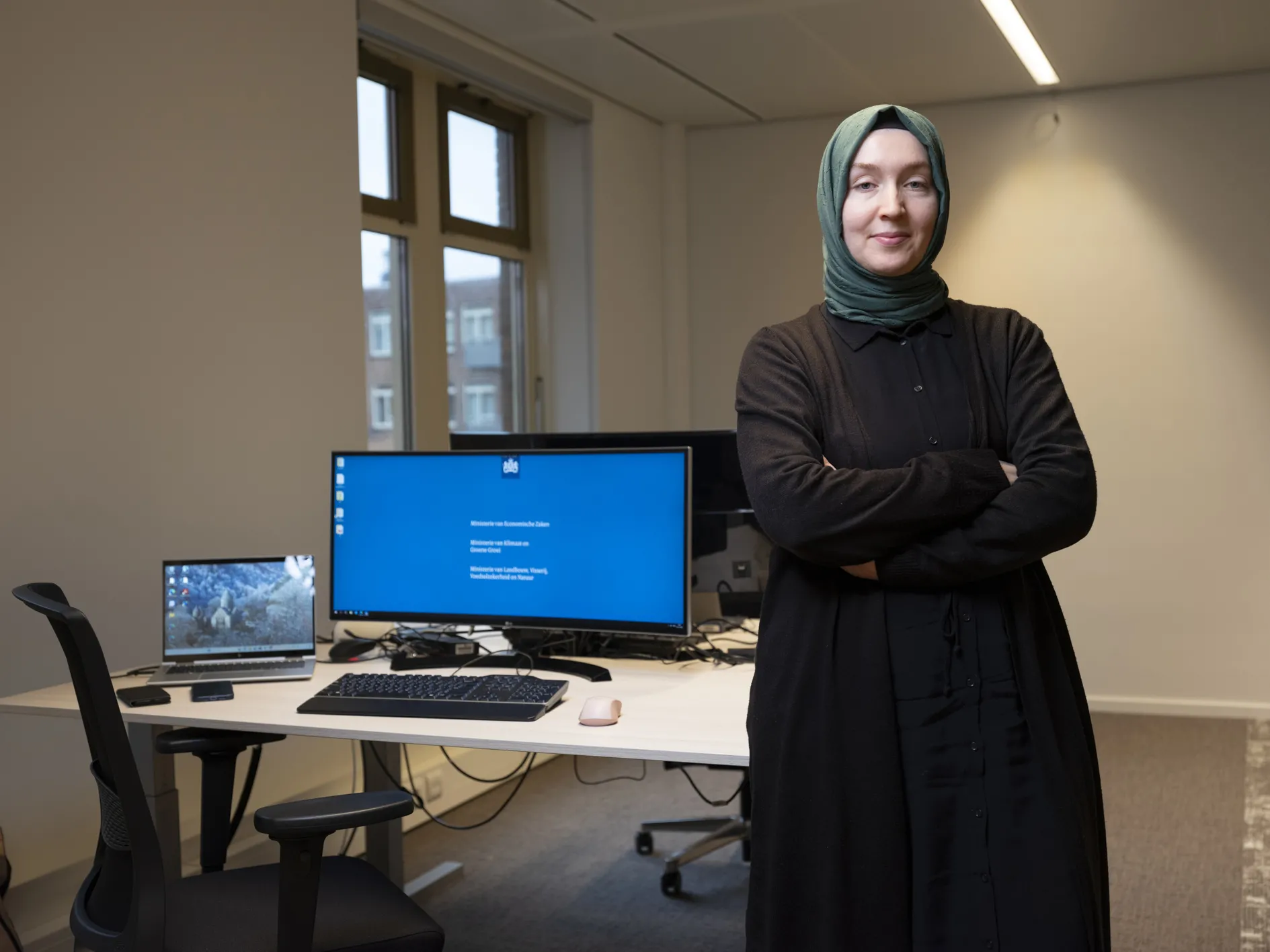 Merve Okur: Vrouw met hoofddoek staat naast laptop op bureau