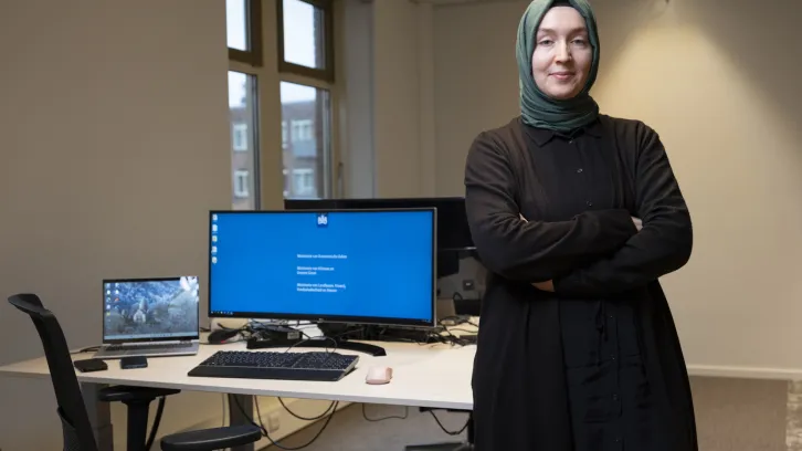 Merve Okur: Vrouw met hoofddoek staat naast laptop op bureau